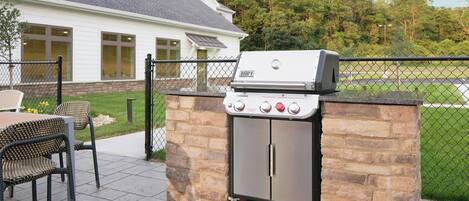 An outdoor grill setup with a stone structure, a chain-link fence, and a house in the background.