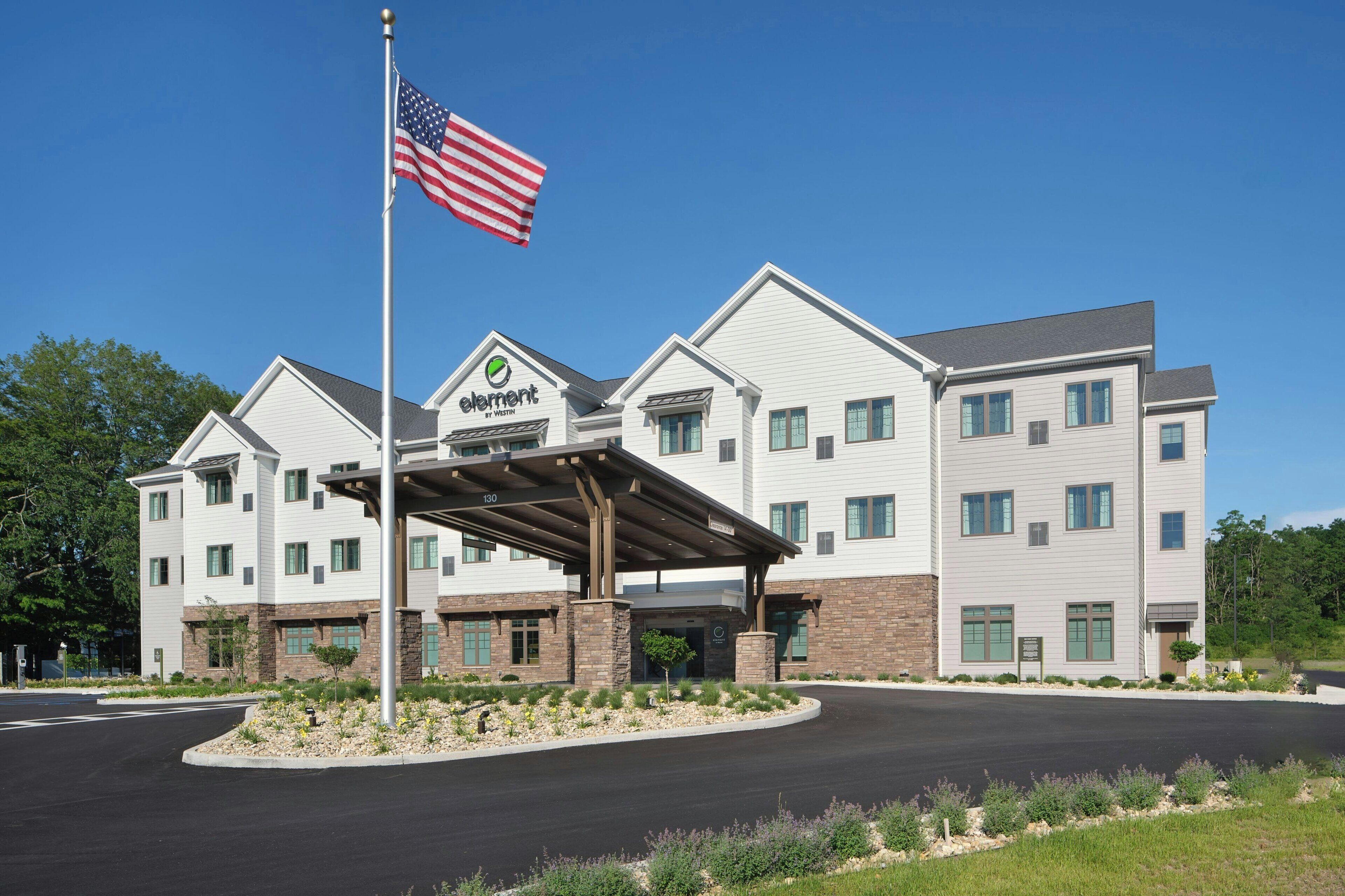 Ein mehrstöckiges Hotel mit überdachter Eingangspartei, einer amerikanischen Flagge und einem begrünten Zugangsbereich.