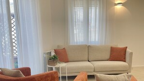 A modern living room with a beige sofa, two orange armchairs, and a small white side table with a plant.