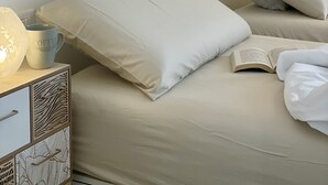 A neatly made bed with a beige duvet, a white pillow, and a book beside it. There's a decorative lamp with a floral design on a bedside table.