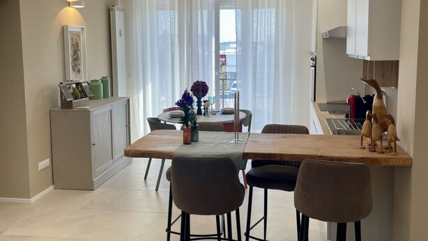 A modern dining area with a wooden table and chairs, a small cabinet, and a decorative vase.