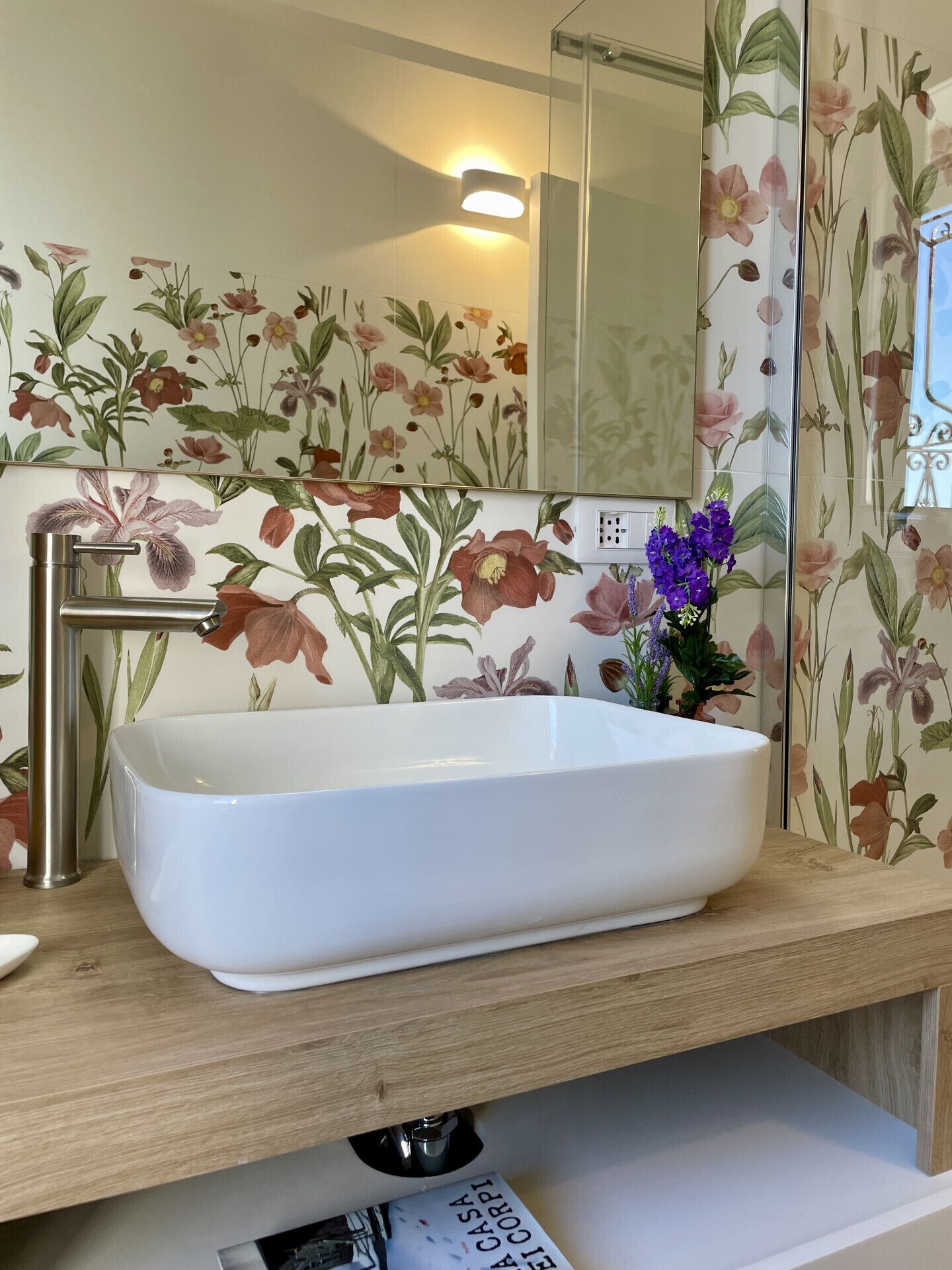 A bathroom with a white sink, a mirror, and floral wallpaper.