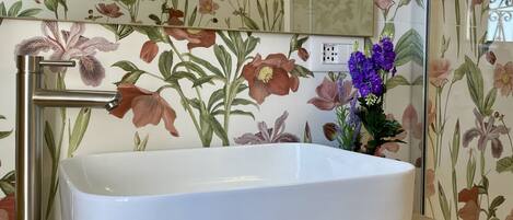 A bathroom with a white sink, a mirror, and floral wallpaper.
