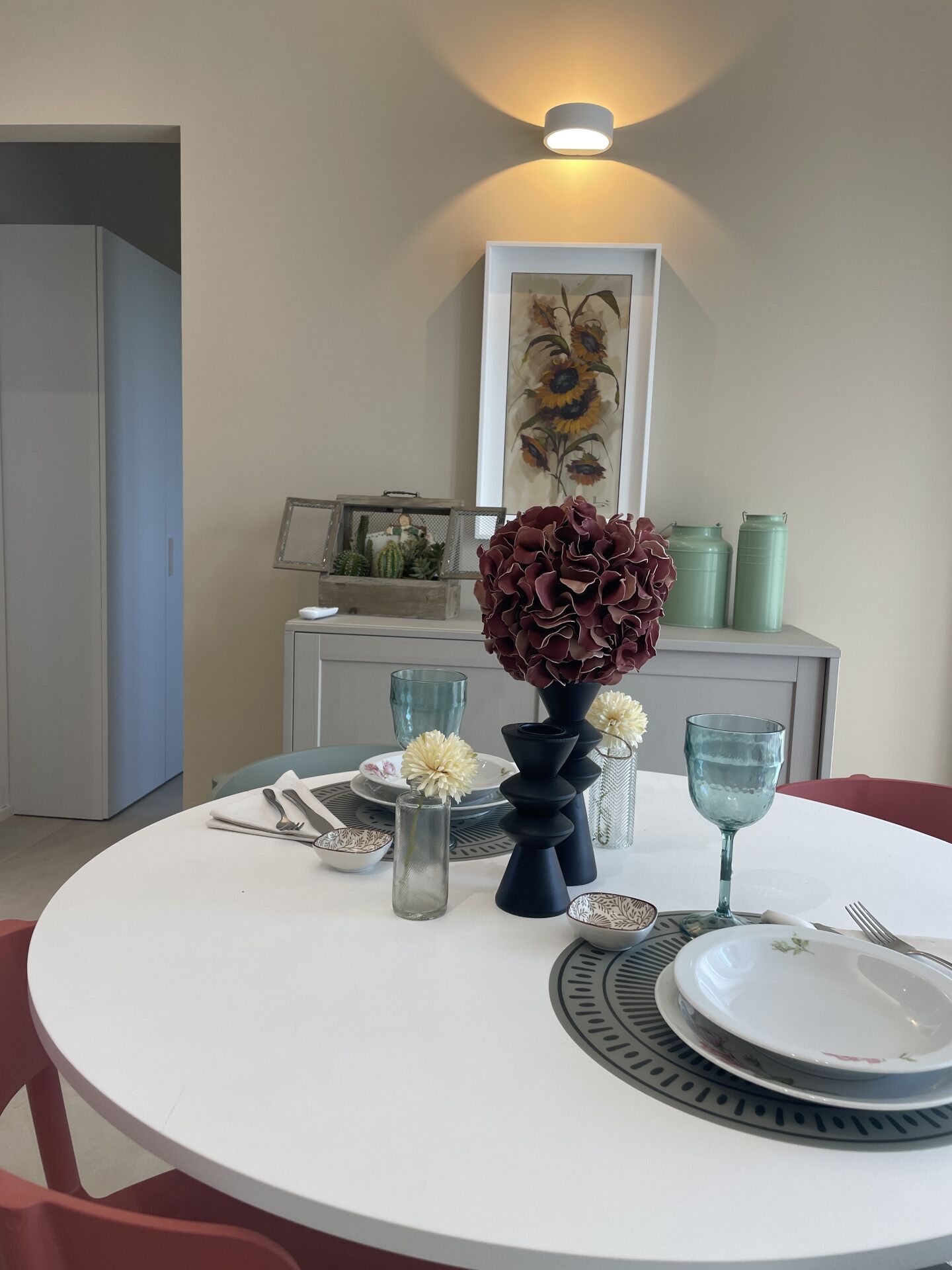 Ein Essbereich mit einem runden Tisch, gedeckt für zwei Personen, mit Blumenvase, Glaskaraffe und Teller mit floralem Dekor.