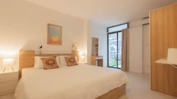 Quarto de hotel moderno com uma cama grande, mesas de cabeceira, um guarda-roupa de madeira e vista para o exterior.