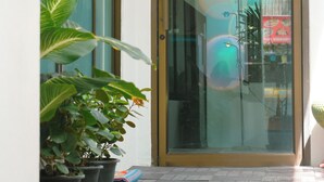 A hotel entrance with a glass door, potted plants, and a tiled floor. - PLACE HOTEL (Karon)