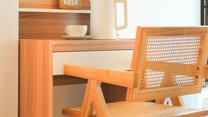 A wooden desk with a white mug, a small decorative item, and a woven chair. - PLACE HOTEL (Karon)