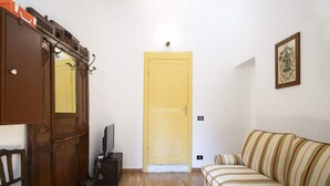 A room with a wooden wardrobe, a yellow door, a striped sofa, and a television on a stand. - Room Nocciola - Affitti Brevi Italia (Genova)