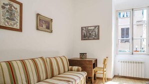 A room with a striped sofa, a wooden table, and a chair. There are three framed pictures on the wall. - Room Nocciola - Affitti Brevi Italia (Genova)