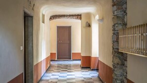 A hallway with a checkered floor, a stone wall on the right, and a door at the end. - Room Nocciola - Affitti Brevi Italia (Genova)