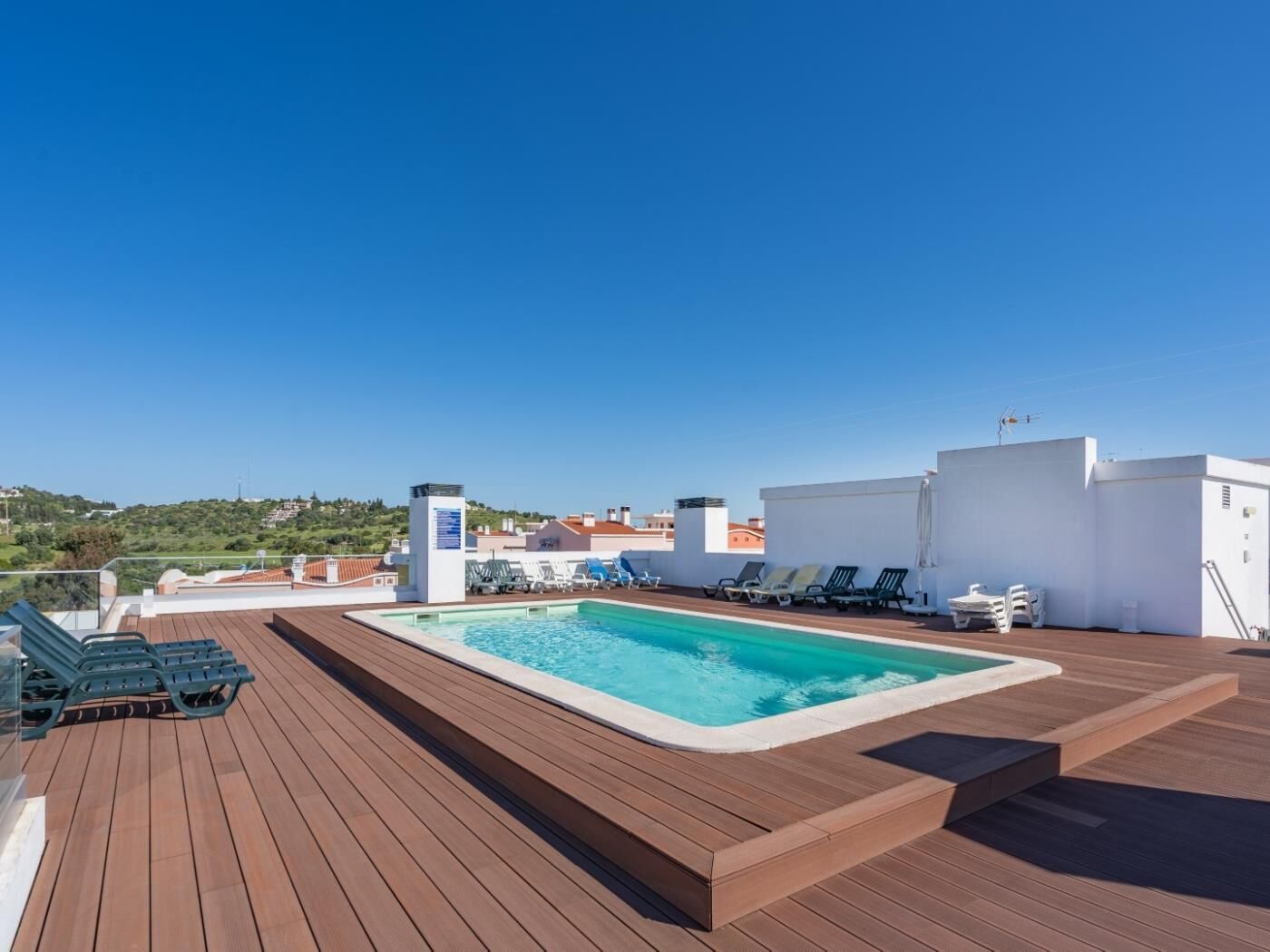 A rooftop pool with wooden decking, lounge chairs, and a clear view of the surrounding landscape.