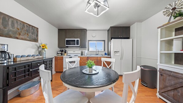 Een moderne keuken met een ronde eettafel, witte stoelen, een inbouwoven, magnetron en koelkast.