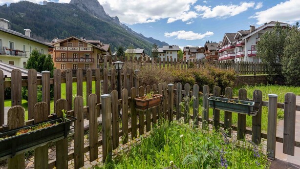 Un village de montagne avec des clôtures en bois, des maisons dotées de balcons et une vue dégagée sur les montagnes en arrière-plan.