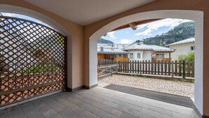 Un espace extérieur abrité, doté d’un sol en pierre, d’une clôture en bois et offrant une vue sur les maisons au loin.