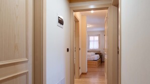 Un couloir étroit, doté d’un plancher en bois, mène à une chambre à coucher qui contient un lit et une fenêtre.
