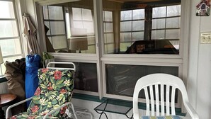 Une pièce donnant sur John Deere Road, avec une chaise blanche à coussin rayé, une chaise à motifs floraux et une petite table.