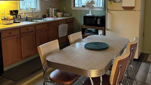 Une cuisine avec des meubles de rangement en bois, une table à manger avec des chaises, un four à micro-ondes et un réfrigérateur.