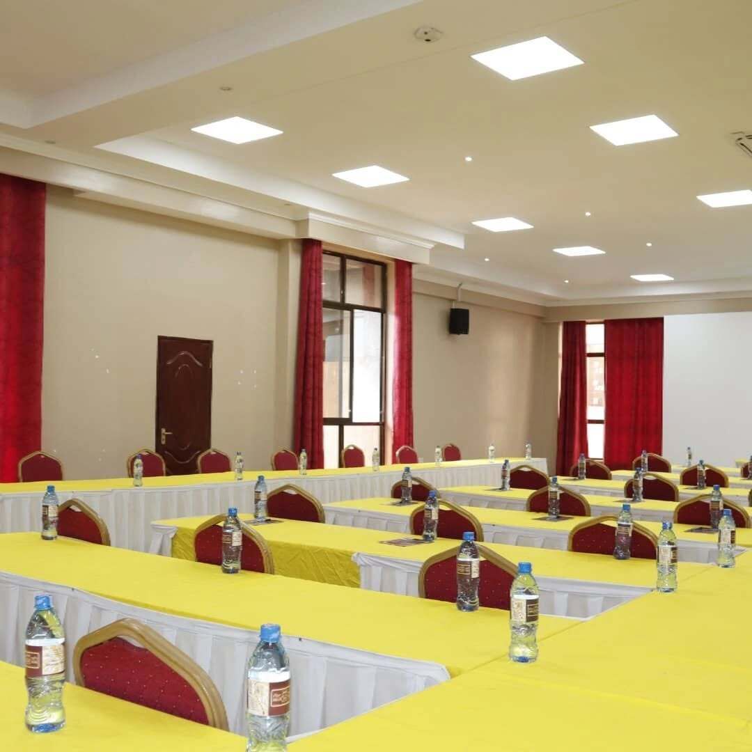 Un salón de conferencias con varias mesas, cada una con mantel amarillo y botellas de agua.
