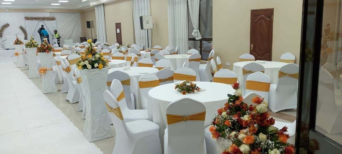 A banquet hall with round tables and white chairs, each with a gold sashed base.