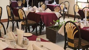 Zona pranzo con tavoli rotondi ricoperti da tovaglie rosse, sedie nere con cuscini gialli e tovaglioli bianchi.