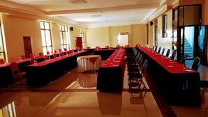 Una sala conferenze con lunghe tavolate, sedie e una lavagna.