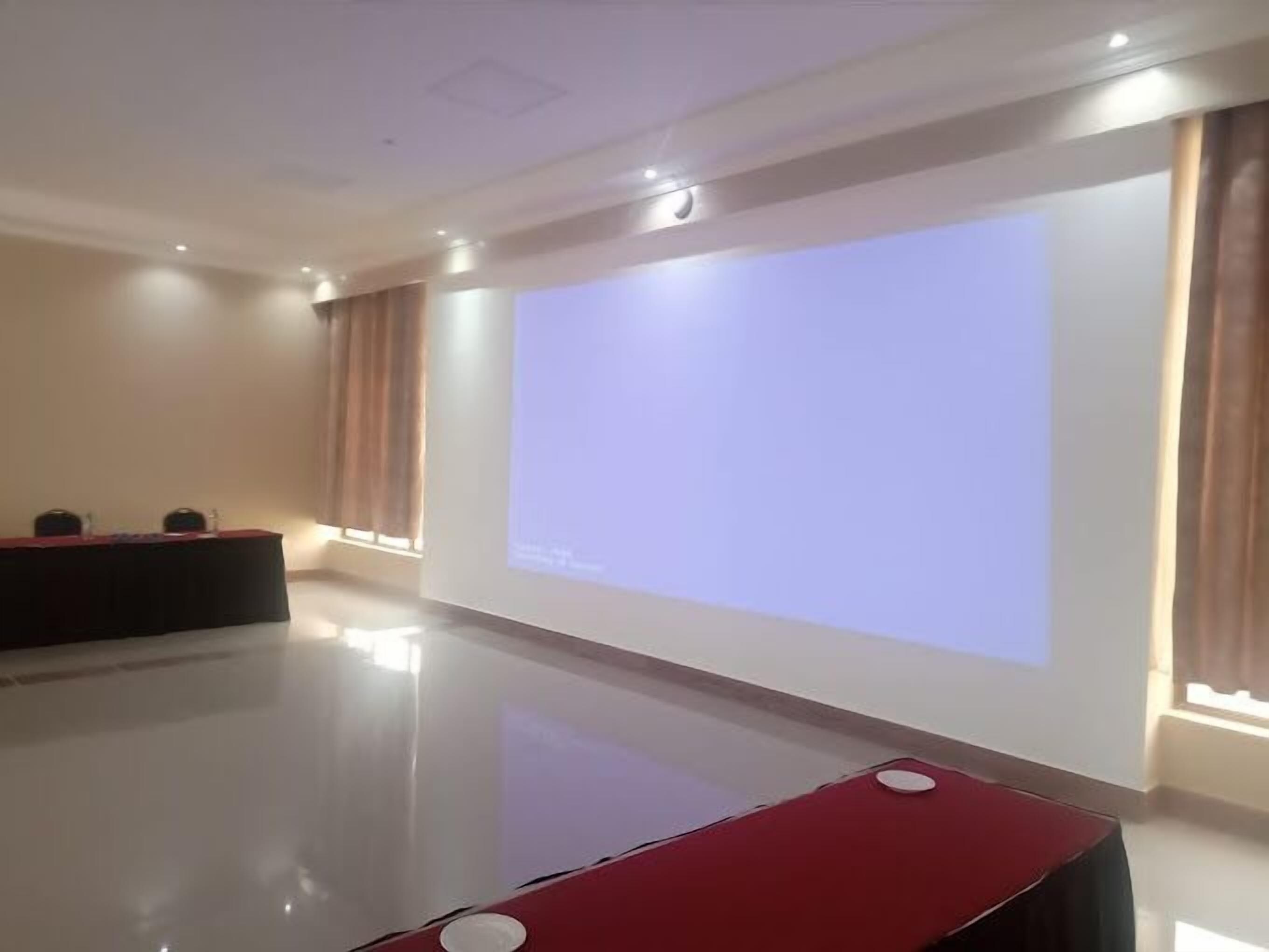 Un salón de conferencias con una pantalla de proyección grande, un atril y una mesa roja.