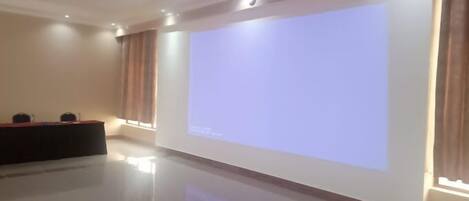 Un salón de conferencias con una pantalla de proyección grande, un atril y una mesa roja.