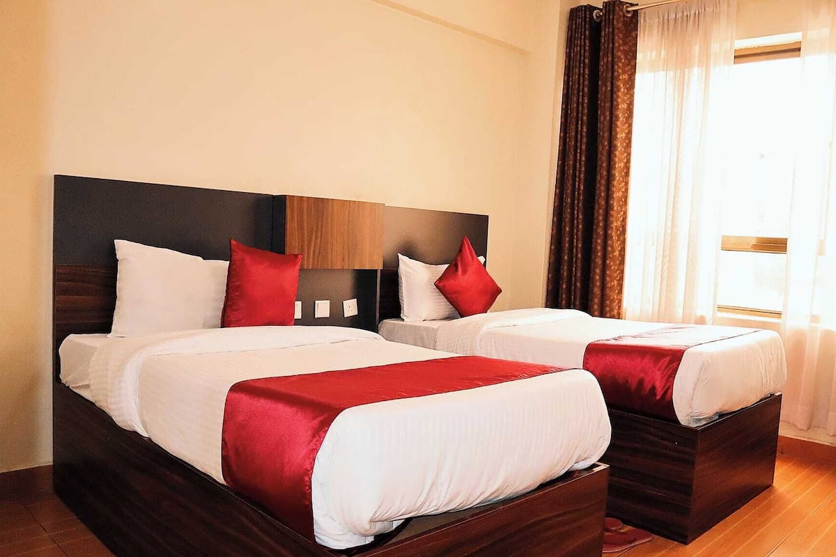 A hotel room with two beds, each with white bedding and red accents.