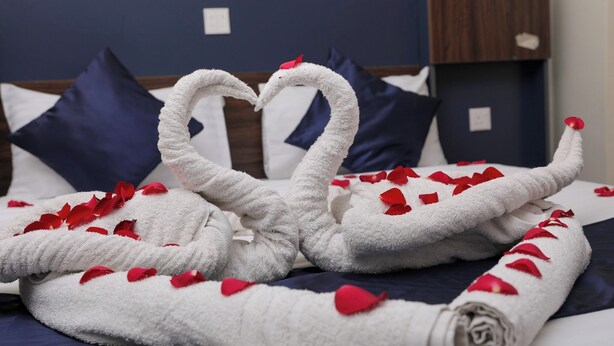 Un letto con un asciugamano bianco disposto a forma di cigno, decorato con petali di rosa rossa.