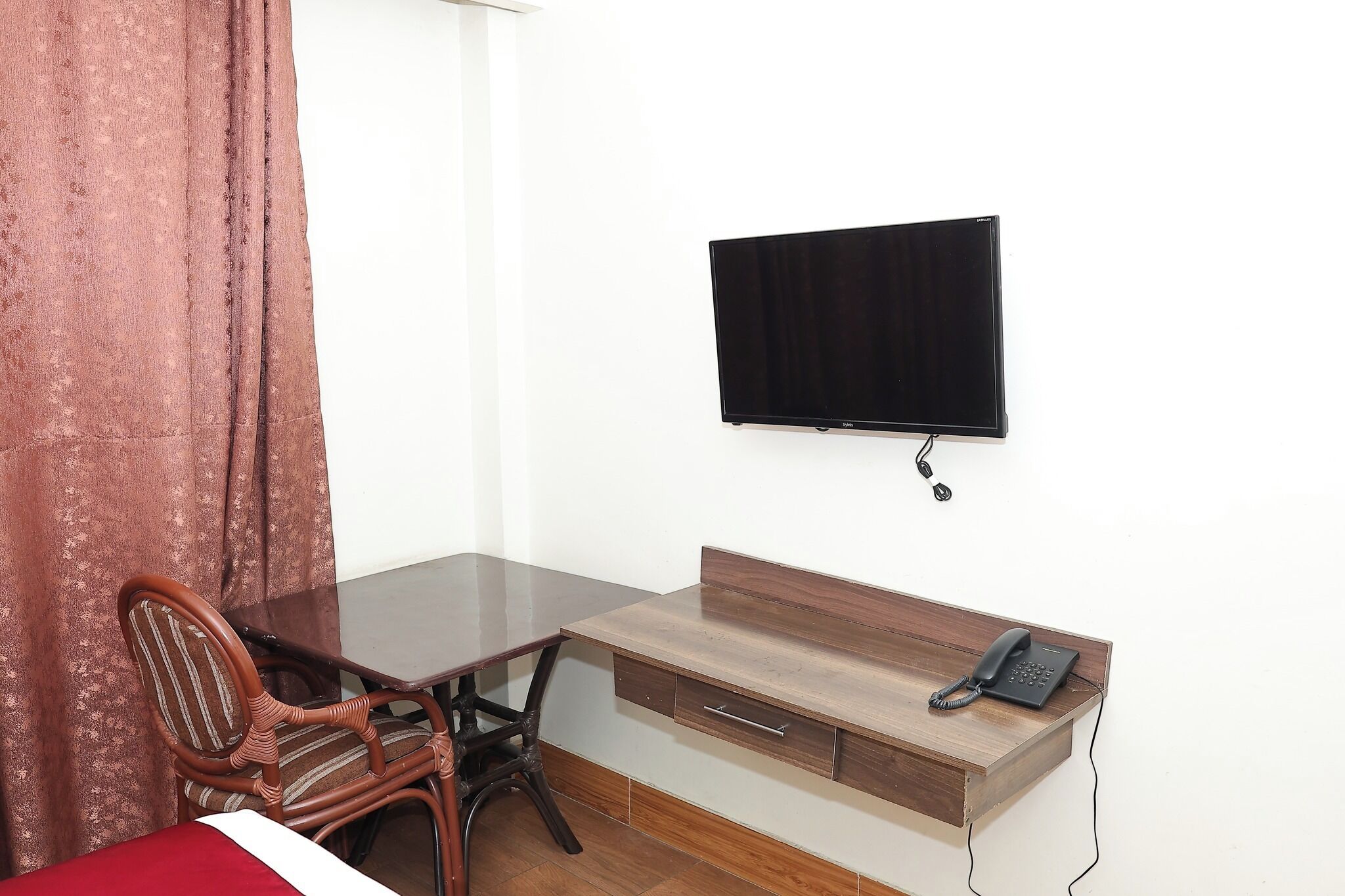 Ein Hotelzimmer mit Holzschreibtisch, einem Sessel, einem Bett, einem an der Wand befestigten Fernseher und einem Telefon auf dem Schreibtisch.