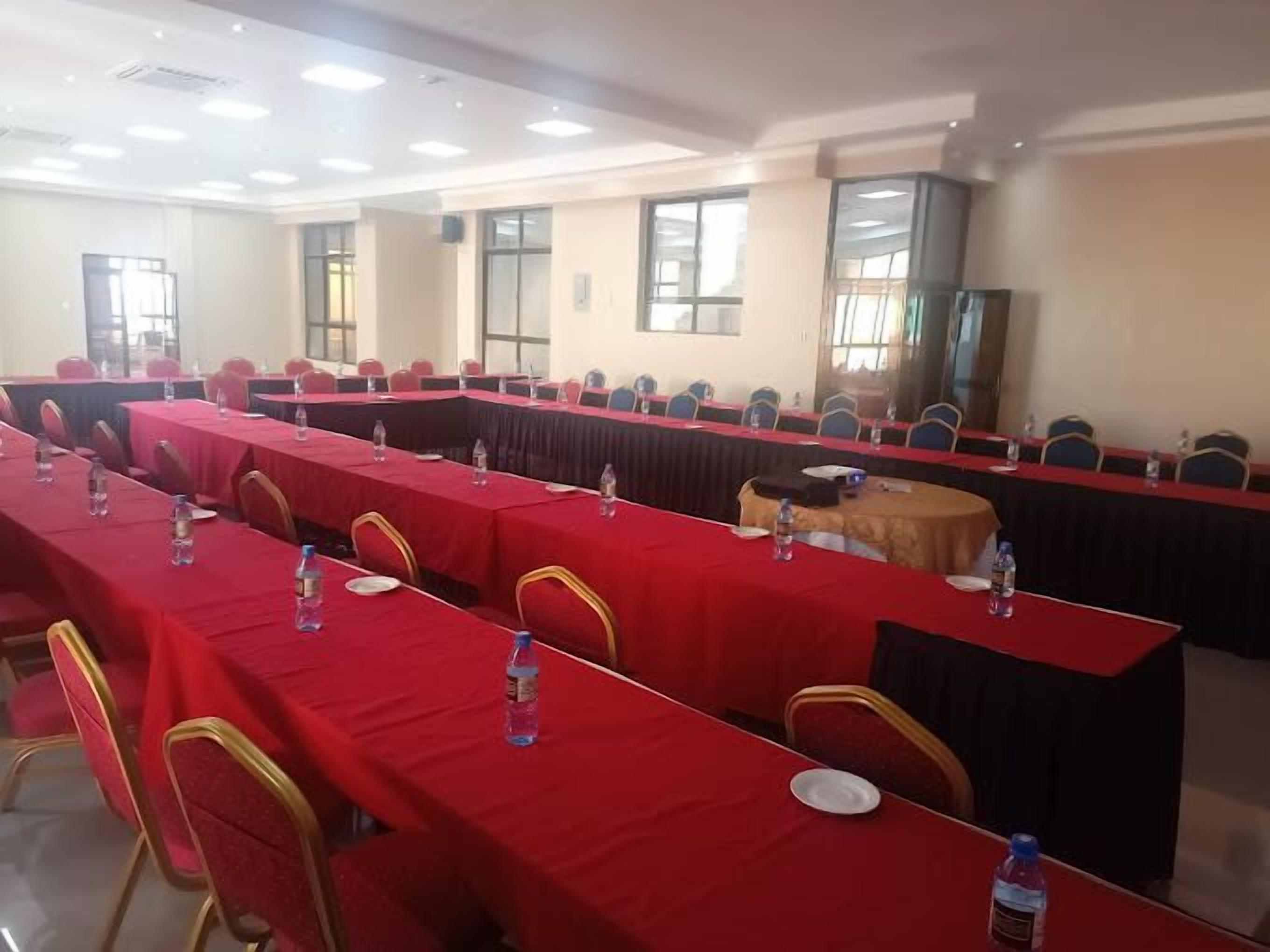 Un salón de conferencias con mesas largas, sillas y botellas de agua.