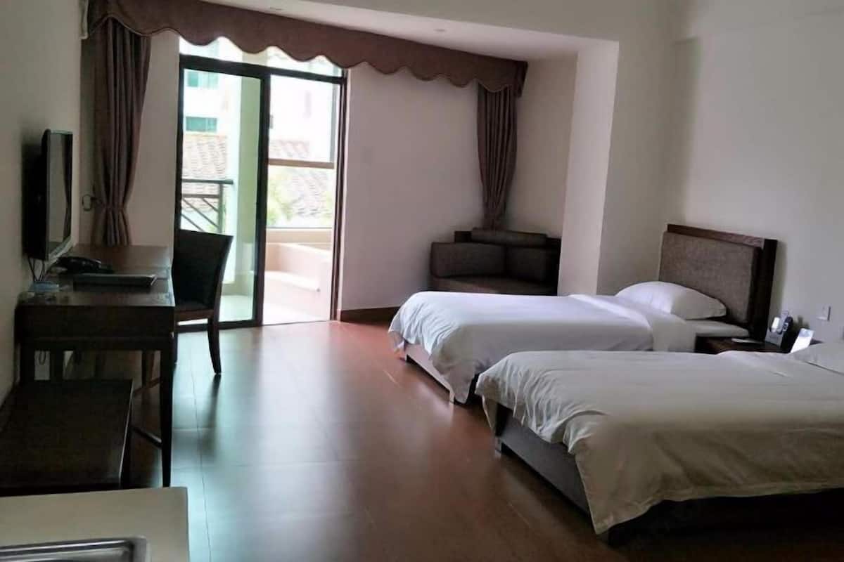 A hotel room with two beds, a desk, a chair, and a television.