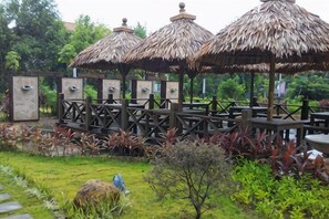 A gazebo with thatched roofs, surrounded by a wooden deck and a garden with various plants. - Wanning Mantening Wenquan Serviced Apartment (Xinglong Town) (Wanning)