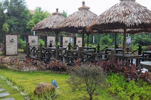 A gazebo with thatched roofs, surrounded by a wooden deck and a garden with various plants.