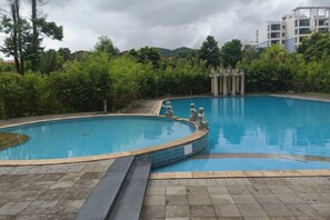 A swimming pool with a tiled edge, surrounded by greenery and a building in the background. - Wanning Mantening Wenquan Serviced Apartment (Xinglong Town) (Wanning)