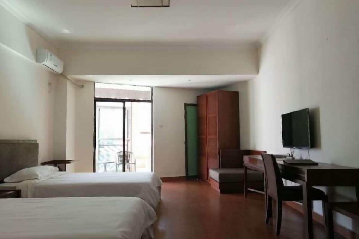 A hotel room with two beds, a desk with a chair, a television, and a sliding door leading to a balcony.