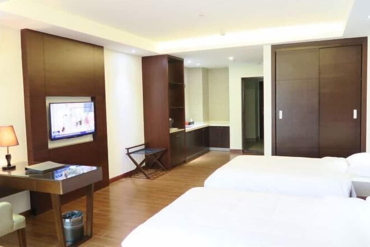 A hotel room with a bed, a desk with a chair, a television, a wardrobe, and a small table with a lamp.