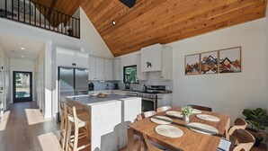A modern kitchen with white cabinets, a large island, and a dining area with wooden furniture.