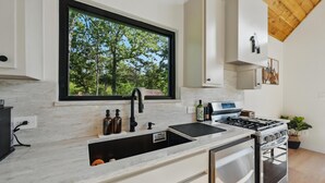 A modern kitchen with a large window, a sink, a stove, and cabinets.