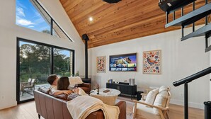 A modern living room with a large window, a wooden ceiling, and a staircase.
