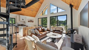A spacious living area with a modern staircase, a cozy seating arrangement, and a large window offering a view of the outdoors.