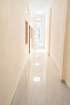 A long, well-lit hallway with a polished floor, wooden doors, and framed pictures on the walls. - Hotel Ajay Palace Ayodhya (Ayodhya)