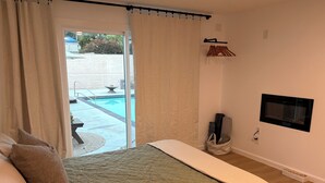A bedroom with a bed, a TV, a window with curtains, and a view of an outdoor swimming pool. - Cozy casita nestled in Laketree Estates, 5 min walk to Monserate Winery. (Fallbrook)