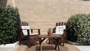A patio area with two wooden chairs and a table, surrounded by a woven rug, against a textured wall. - Cozy casita nestled in Laketree Estates, 5 min walk to Monserate Winery. (Fallbrook)