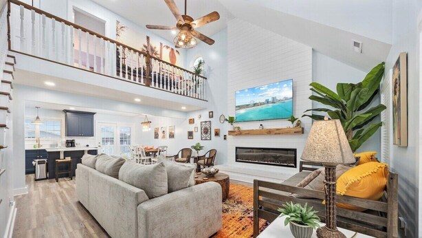 A spacious living area with a high ceiling, a balcony, a fireplace, and a large TV.