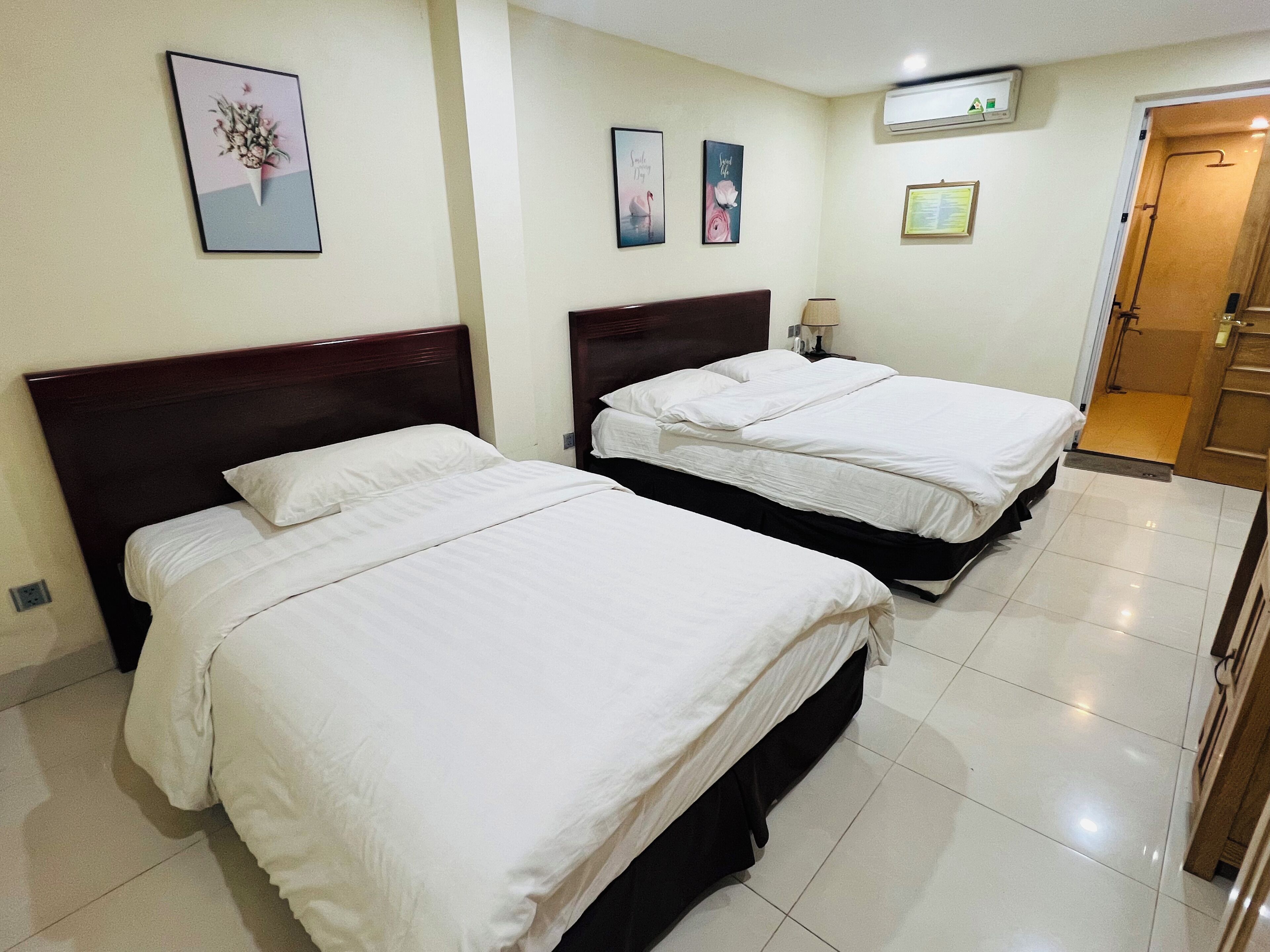 A hotel room with two beds, a small bedside table with a lamp, and a door leading to a bathroom.