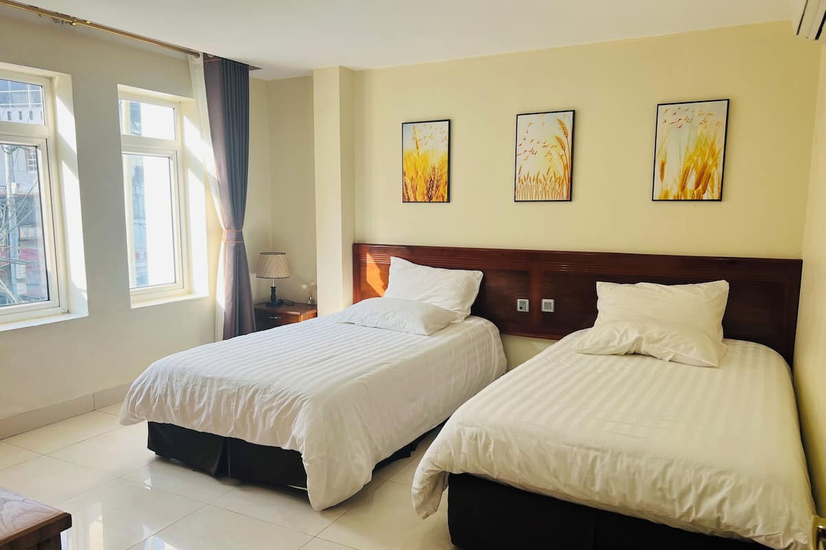 A hotel room with two beds, a nightstand, a lamp, and three wall-mounted paintings.