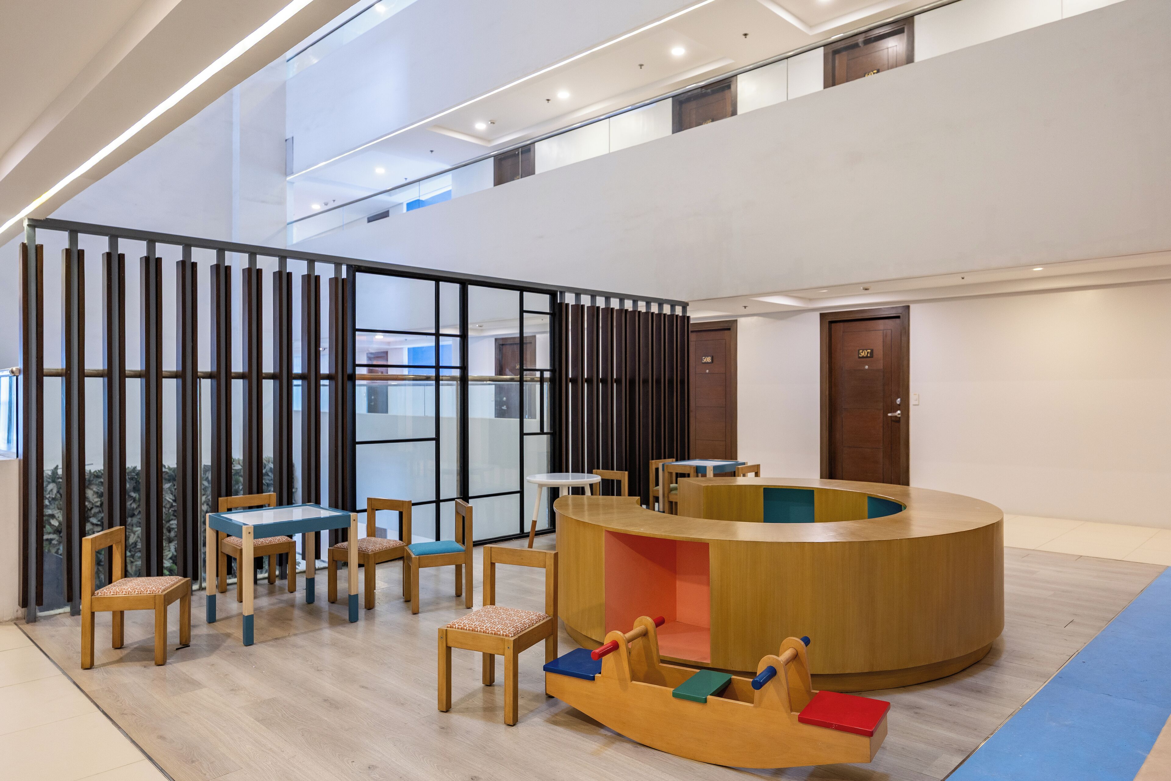 Un espacio interior moderno con una zona de juegos de madera, una mesa redonda y un separador de vidrio.