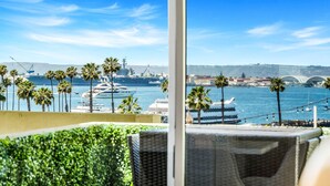 Vista desde un balcón con vistas a un puerto deportivo con yates, palmeras y un puente al fondo.