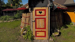A rustic wooden structure with a thatched roof, a heart-shaped window, and a red door. - Glamping at “The Nest” in Müritz National Park (Penzlin)